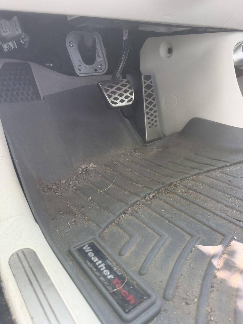 Driver footwell before detailing — dirt and debris ground into the floor mat around the pedals